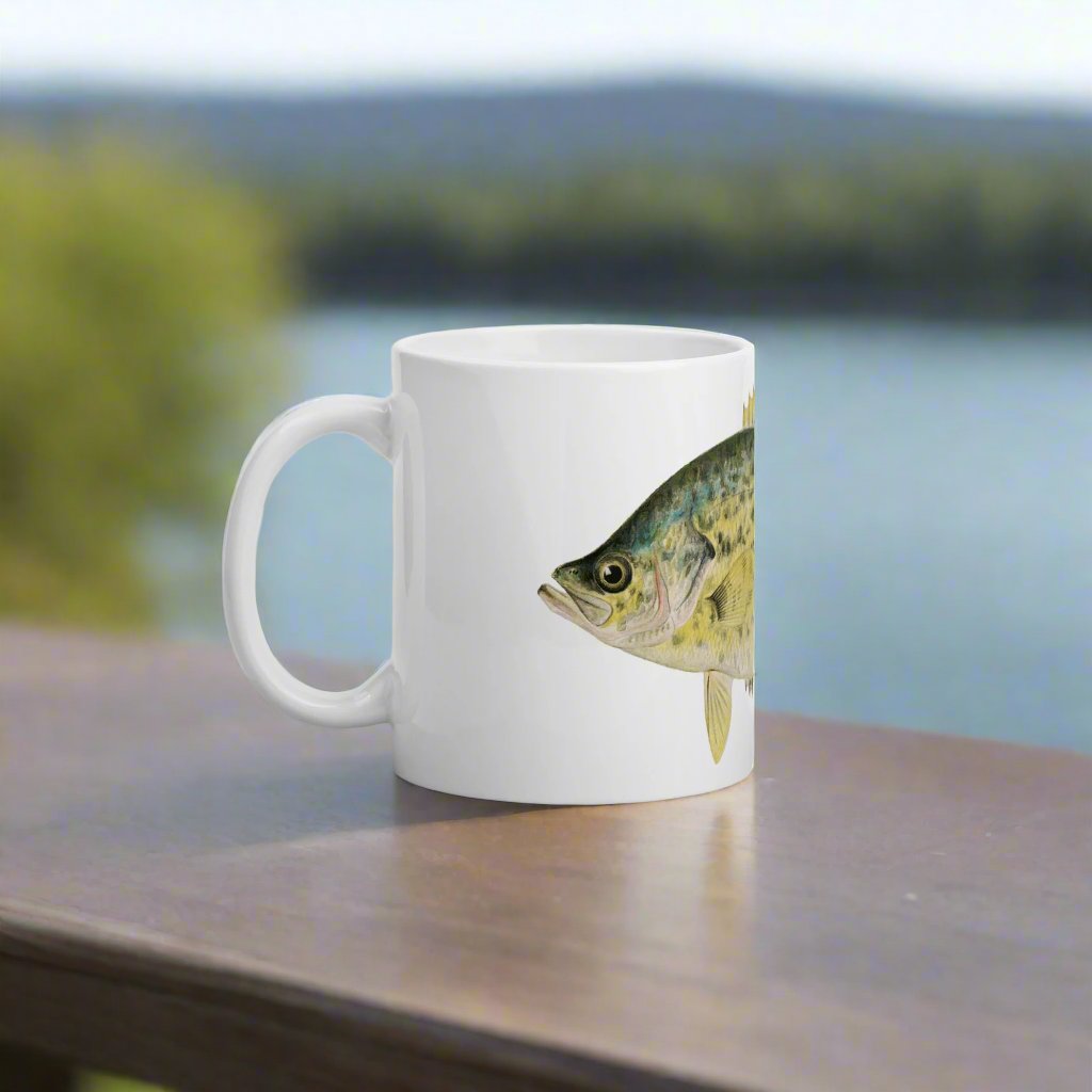 crappie design on a coffee mug sitting on a table outside with a waterfront view