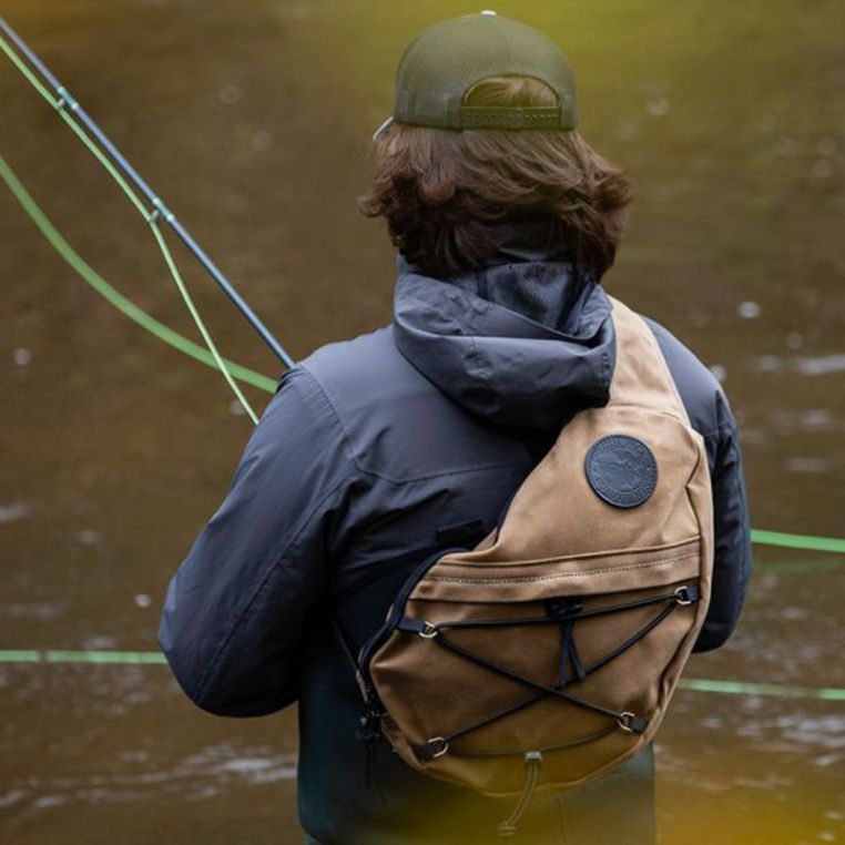Fly angler wearing the Duluth Pack 16L Canvas Sling Pack while fishing