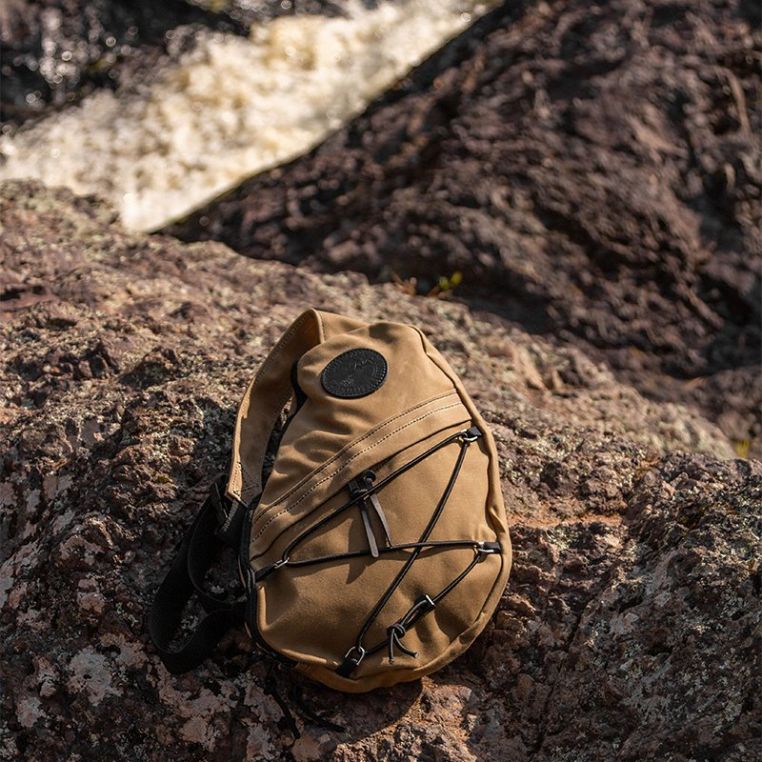 Tan Duluth Pack 16L Canvas Sling Pack displayed on a rock outdoors