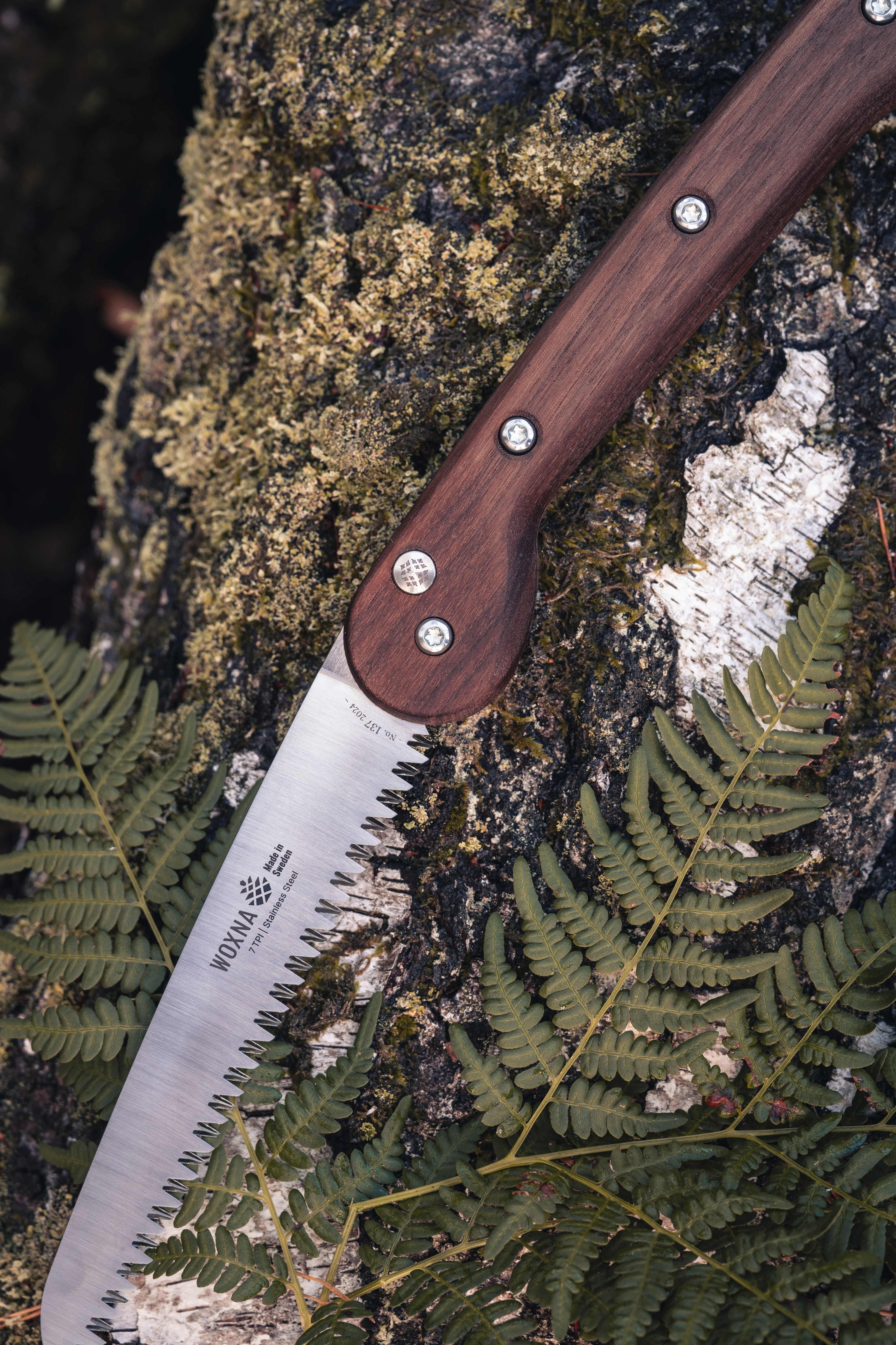 Woxna Ljusnan 7-inch foldable saw in an outdoor setting with walnut handle and stainless steel blade